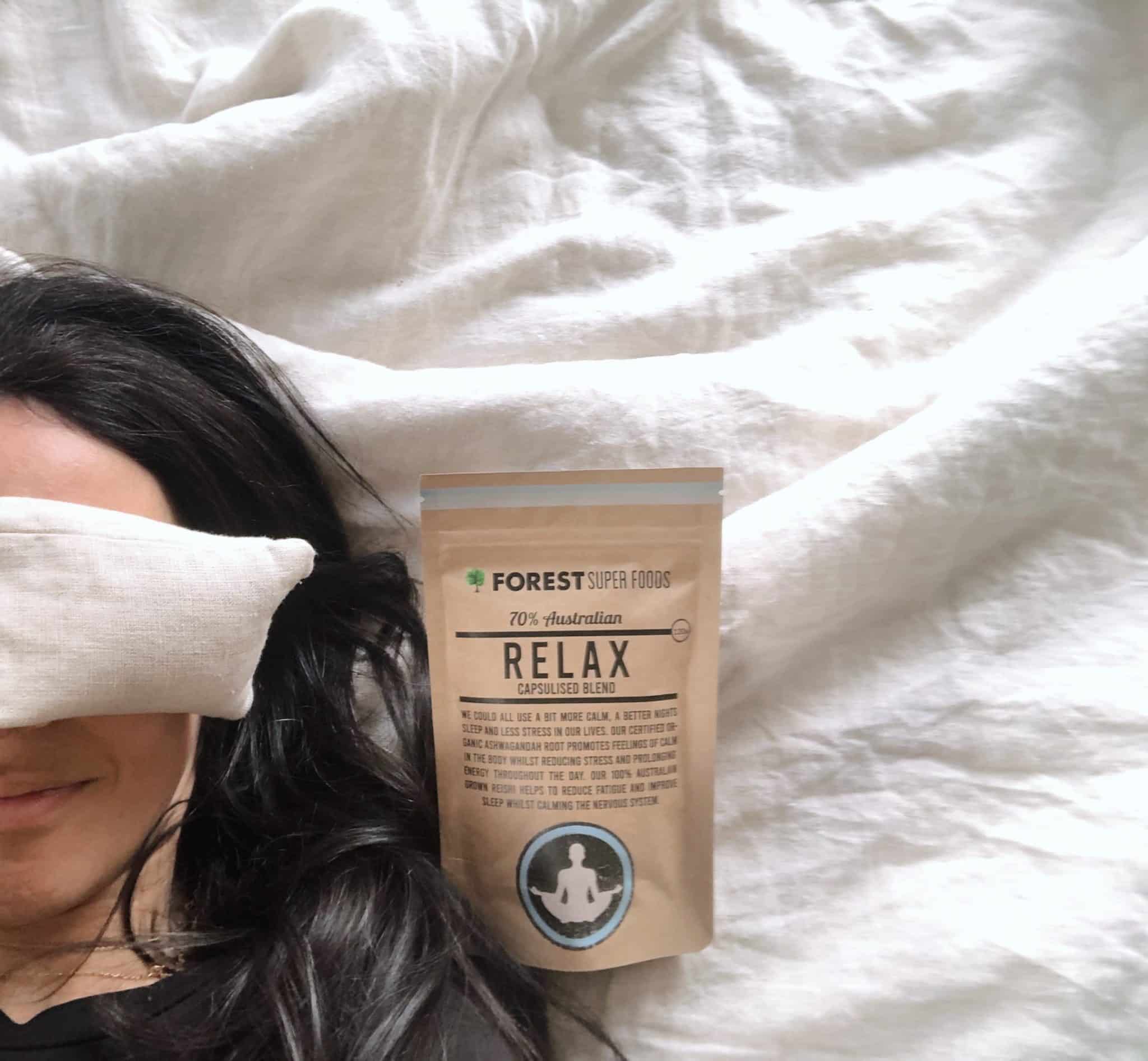 Rest & Relax Bundle natural supplement pouch on white bedding beside person resting with eye pillow over face